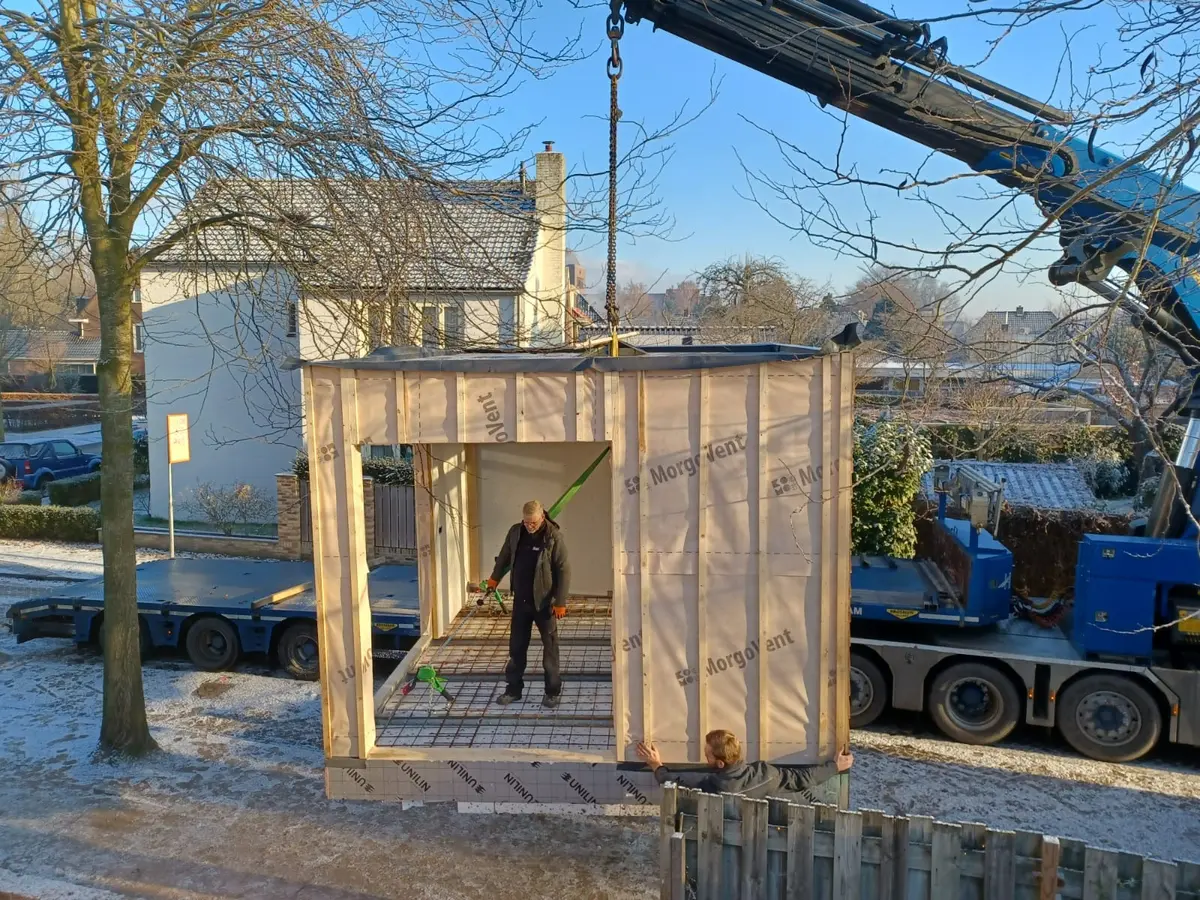 Prefab aanbouwmodule hangt aan de kraan, met een monteur binnenin