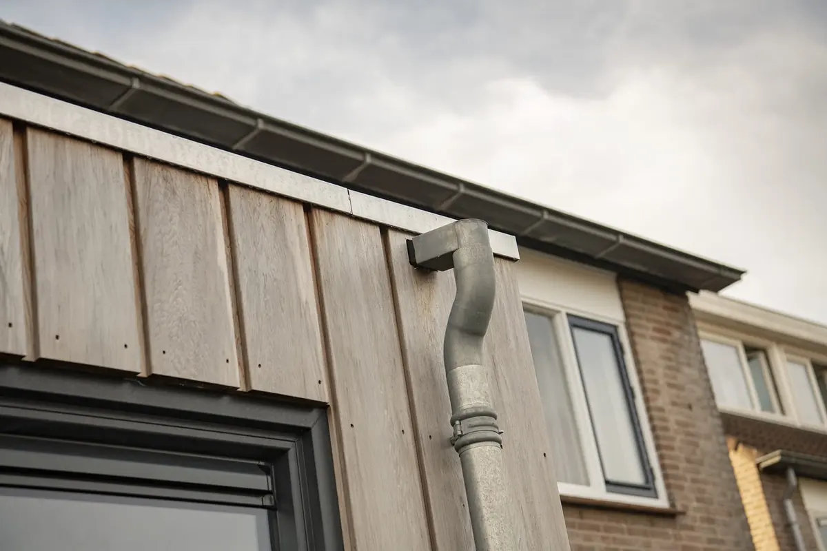 Dakrand en verticale houten gevelbekleding met regenpijp naast de bestaande gevel
