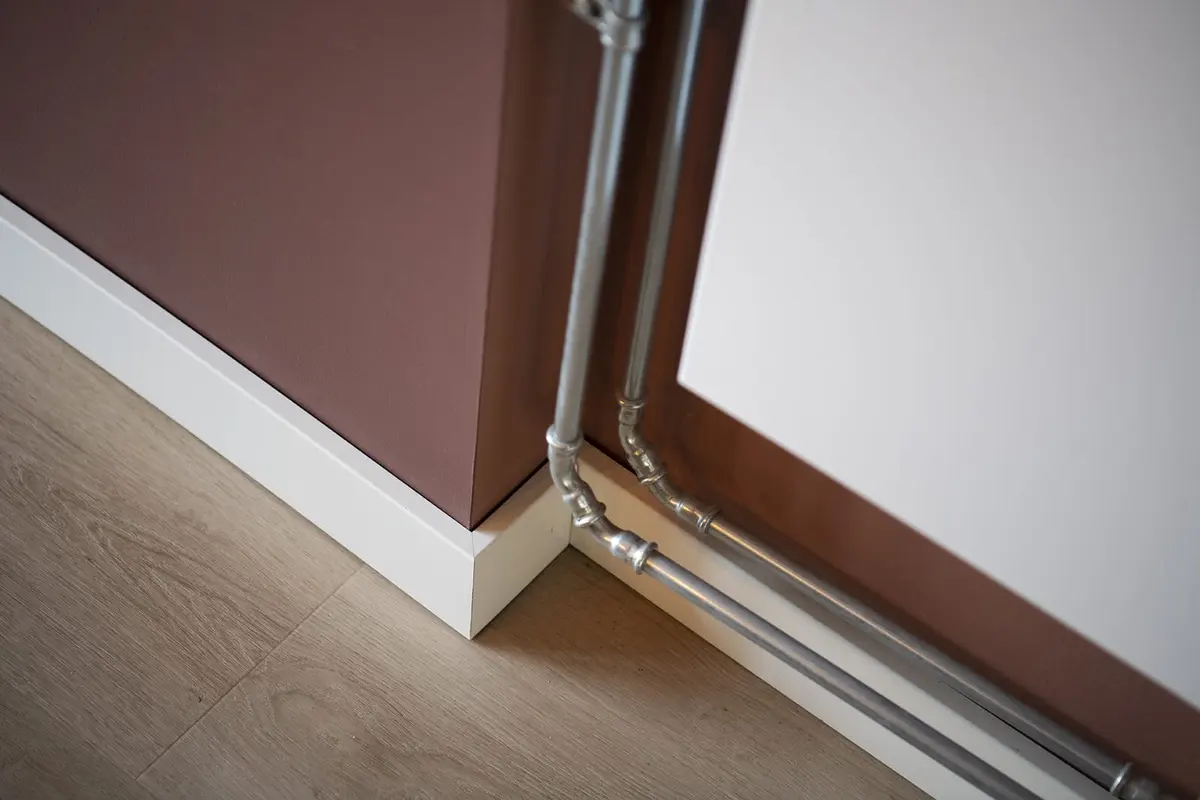 Detail van de plint en het leidingwerk langs de wand in de aanbouw