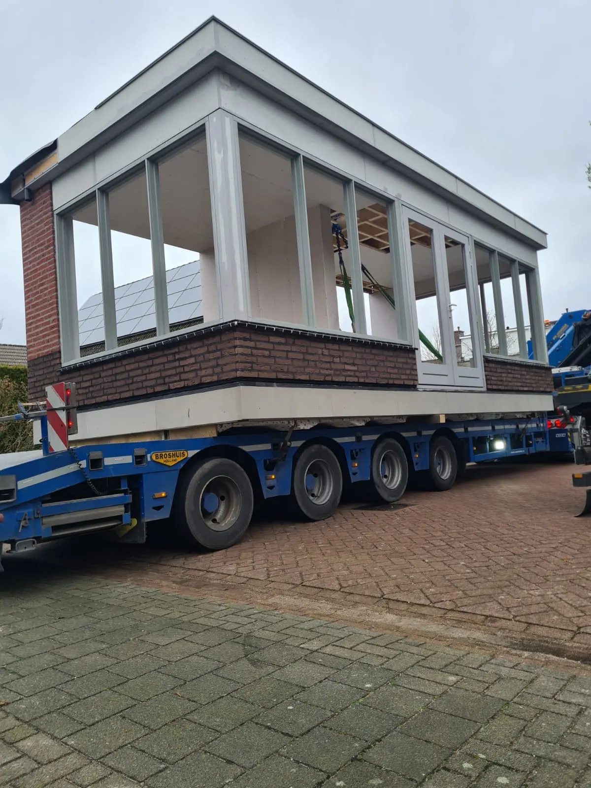 Prefab aanbouw met witte kozijnen en bakstenen plint op een dieplader