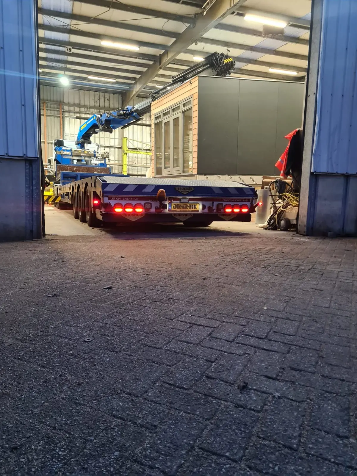 Vrachtwagen met prefab aanbouw rijdt de werkplaats uit
