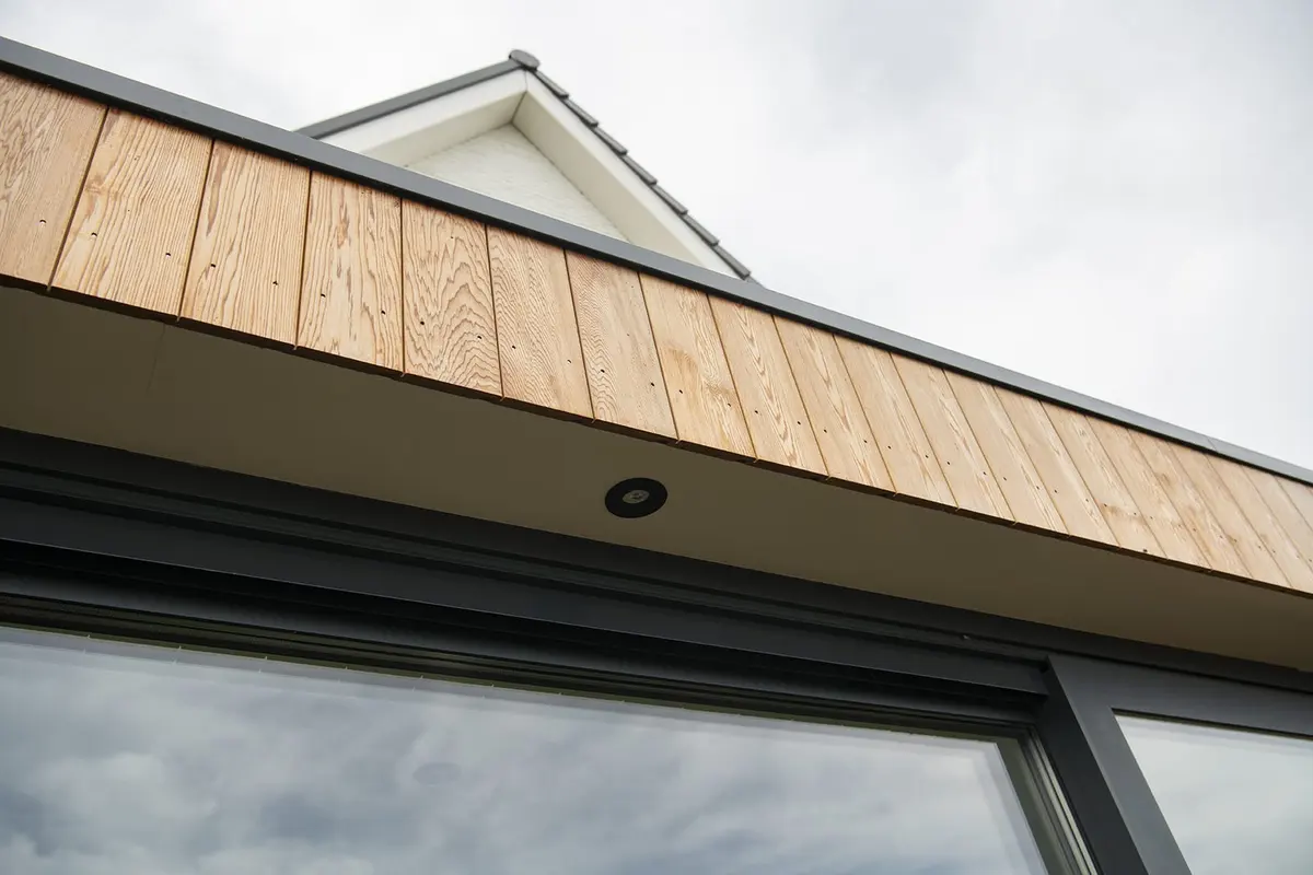 Houten dakrand met inbouwspots boven de glazen pui