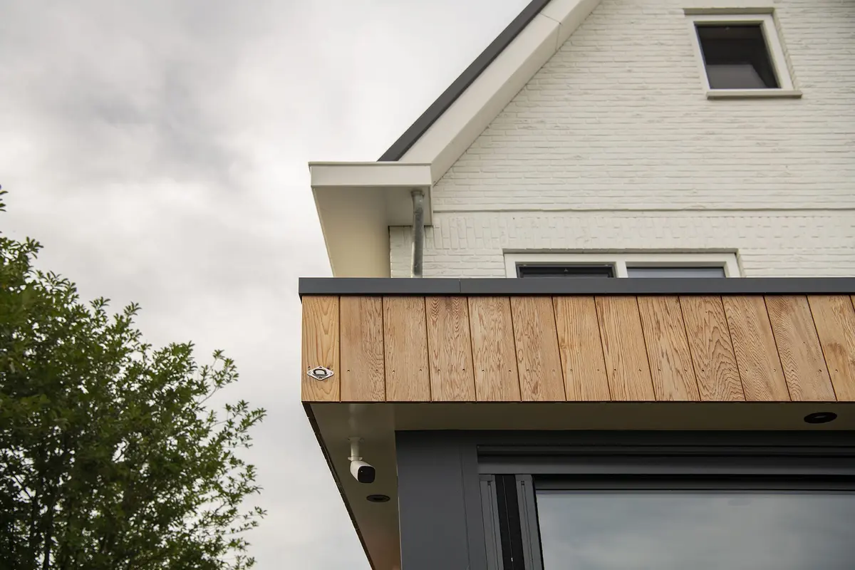 Overstek van de aanbouw met houten dakrand tegen een bewolkte lucht