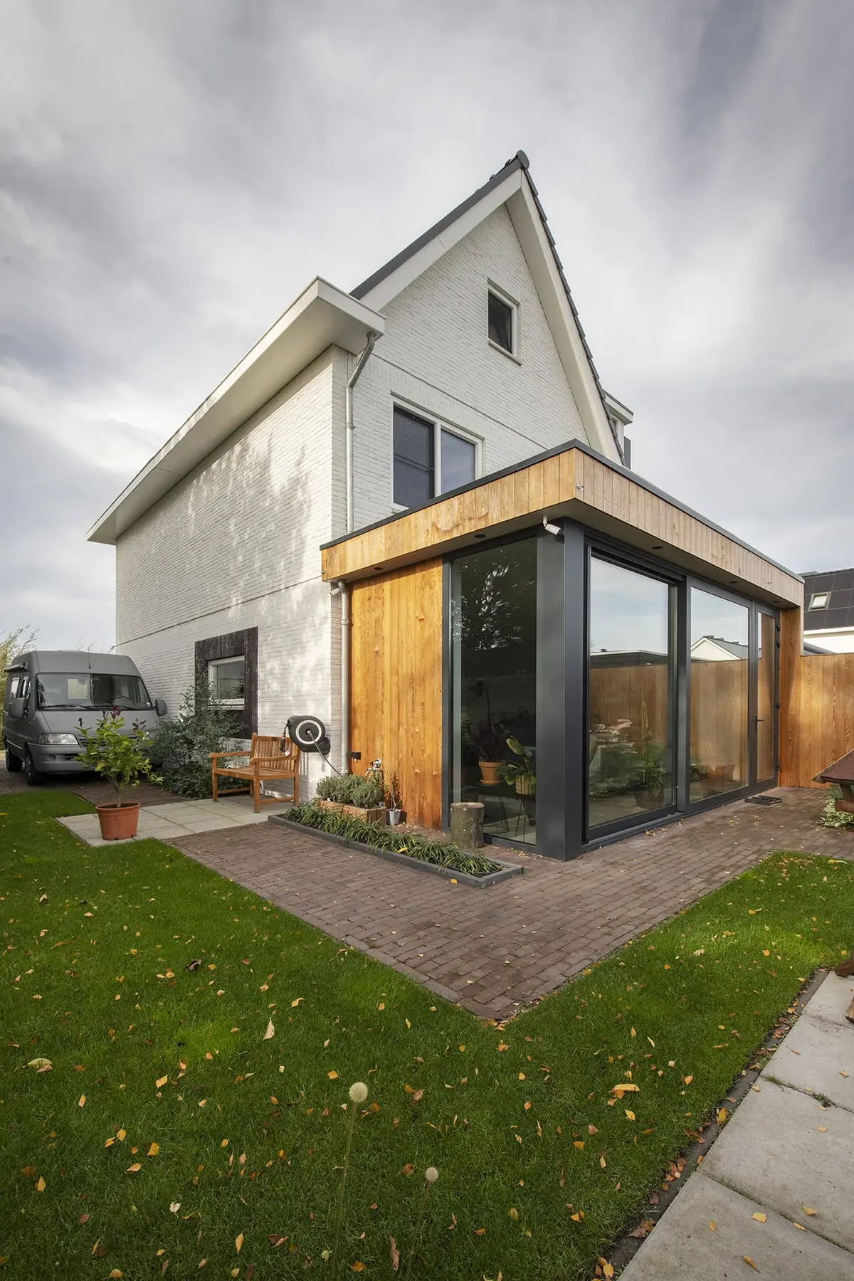 Hoekaanbouw met glazen gevel en houten dakrand aan een witte woning in Vlijmen