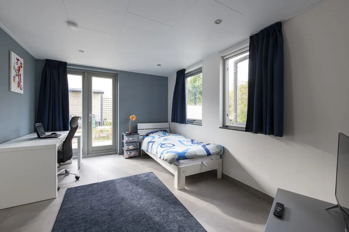 Slaapkamer in de zorgaanbouw met bed, bureau en openslaande deuren naar de tuin