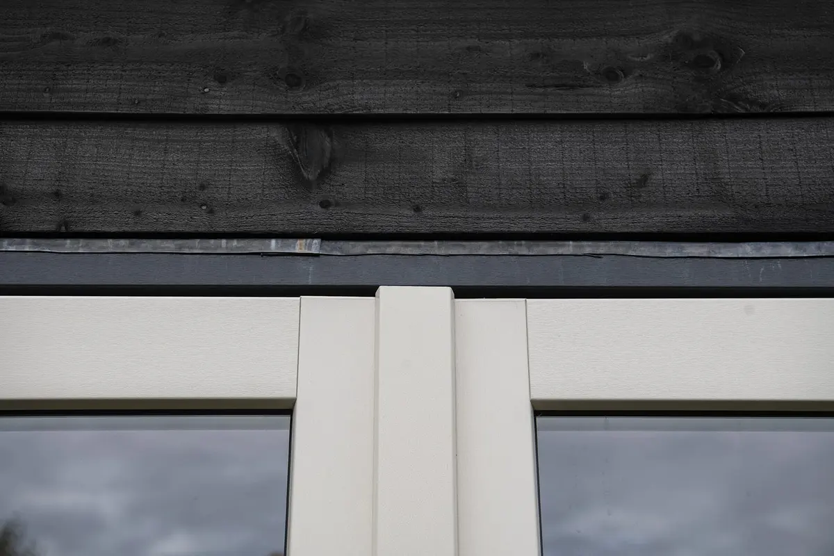 Detail van het witte kozijn onder de zwarte gevelbekleding