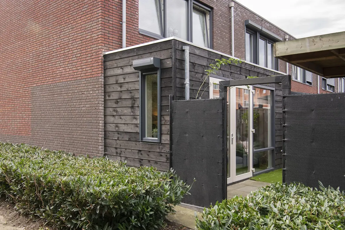 Uitbouw met zwarte houten gevel aan een bakstenen hoekwoning