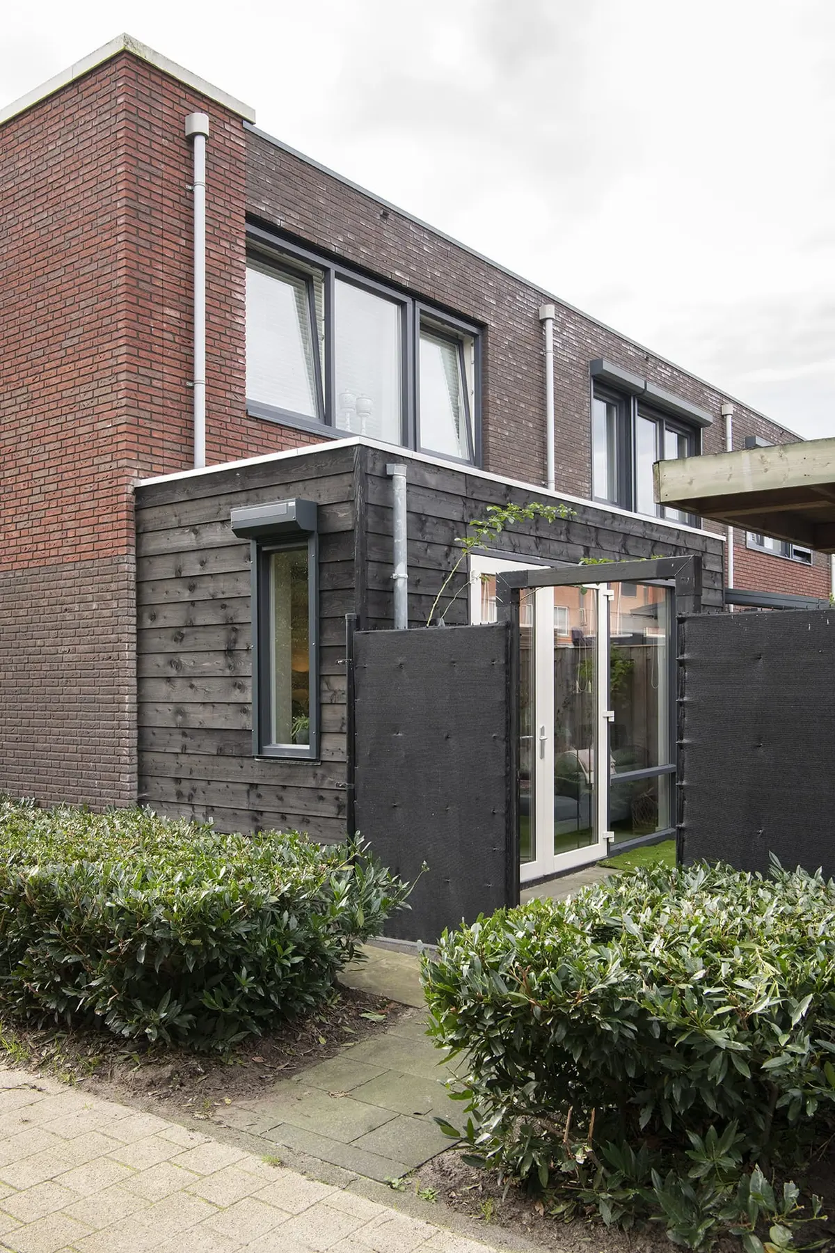 Uitbouw met zwarte houten gevel en tuindeur aan een bakstenen hoekwoning