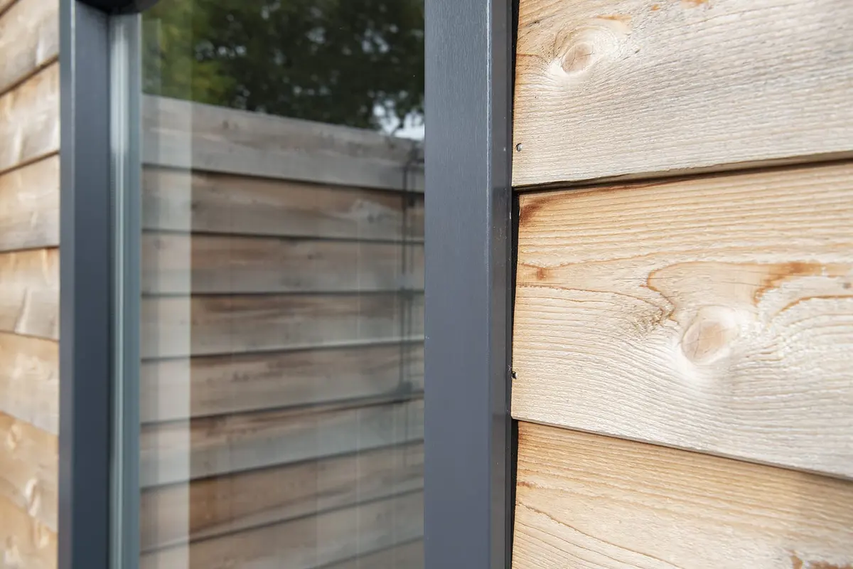 Detail van glas, antraciet kozijn en cederhouten gevelbekleding