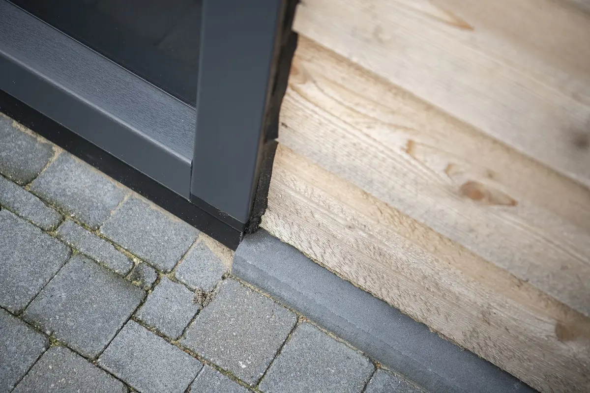 Onderaansluiting van kozijn en houten gevel op de bestrating